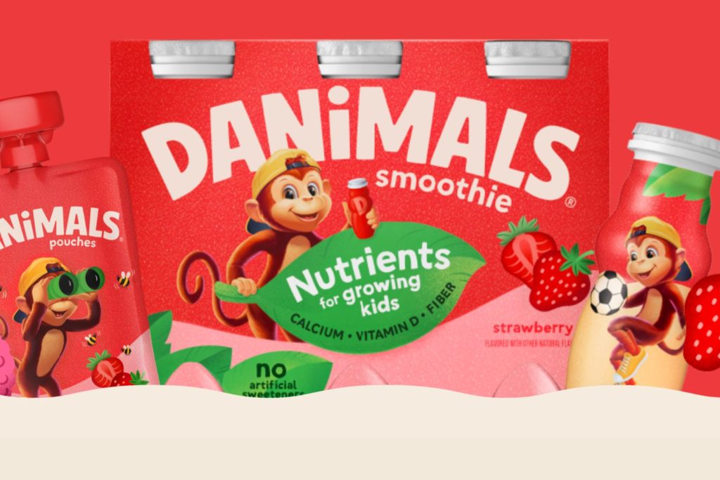 A playful monkey character holds a smoothie bottle in front of colorful packaging that emphasizes nutrients, alongside illustrations of strawberries and playful elements, featured in the Danimals MAGNA-TILES Sweepstakes
