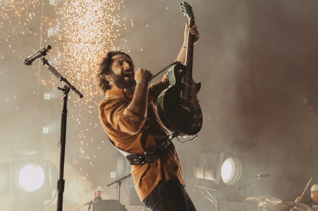 A musician passionately performs on stage, holding a green electric guitar while singing into a microphone, with sparks illuminating the background, creating an energetic atmosphere, featured in the Visit Music City Thomas Rhett Sweepstakes