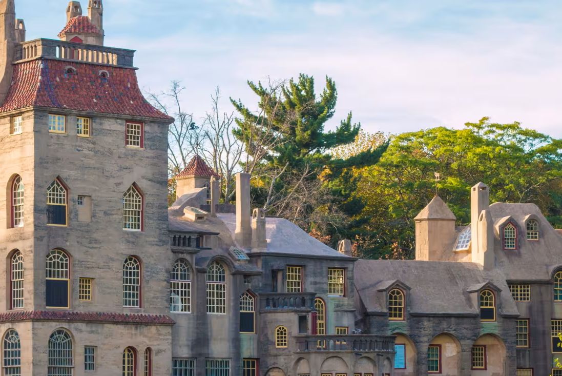 A whimsical castle with a mix of architectural styles features tall towers and intricate windows, surrounded by lush trees and foliage under a clear blue sky, featured in the Visit Bucks County Getaway Sweepstakes